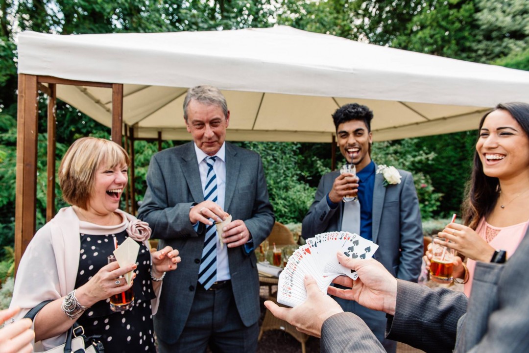 Card fan trick at outdoor drinks reception with laughing guests
